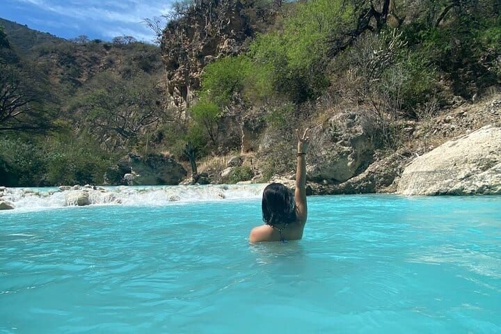 A swimmer with one arm raised in the bright turquoise river