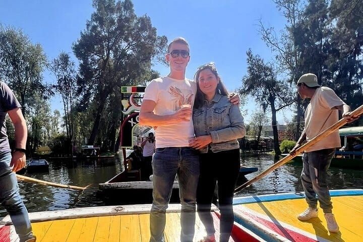 Una pareja con sus bebidas a bordo mientras el remero impulsa la trajinera