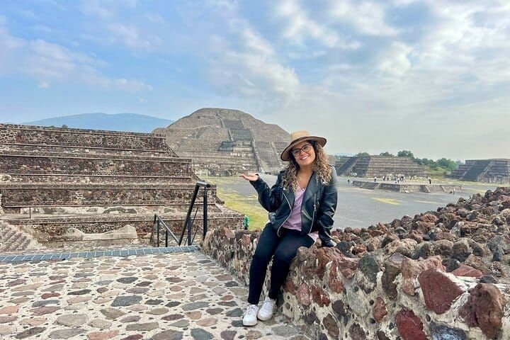 Una visitante posa sobre el muro de piedra con la Pirámide de la Luna detrás